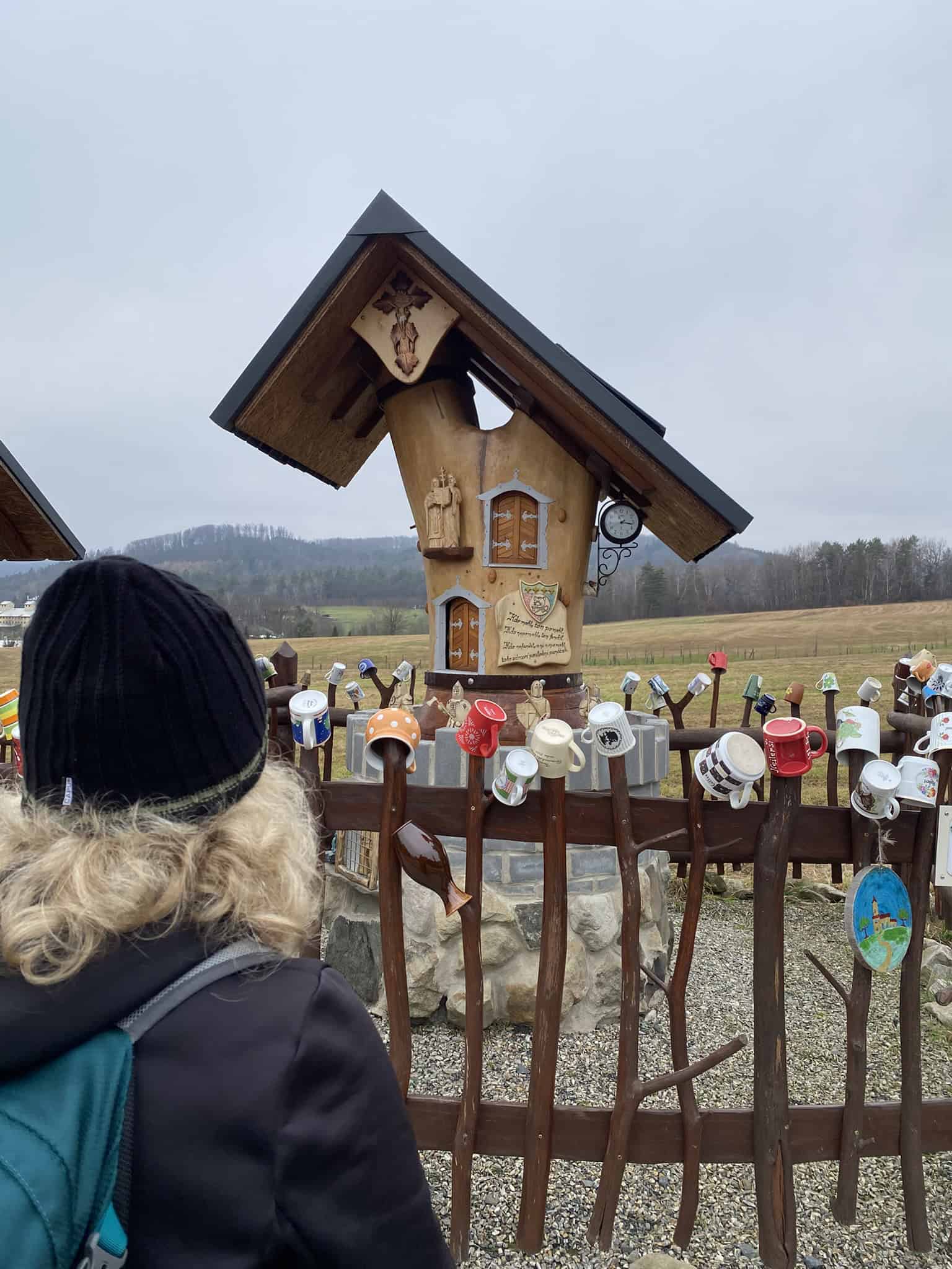 Zvláštní umělecké dílo s malými dvířky a plůtkem osazeným hrnečky.