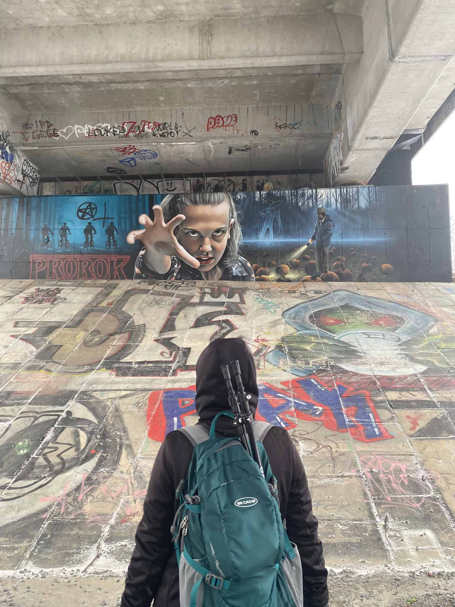 Účastnice výpravy zírá na detailní graffiti pod mostem, které připomíná seriál Stranger Things.