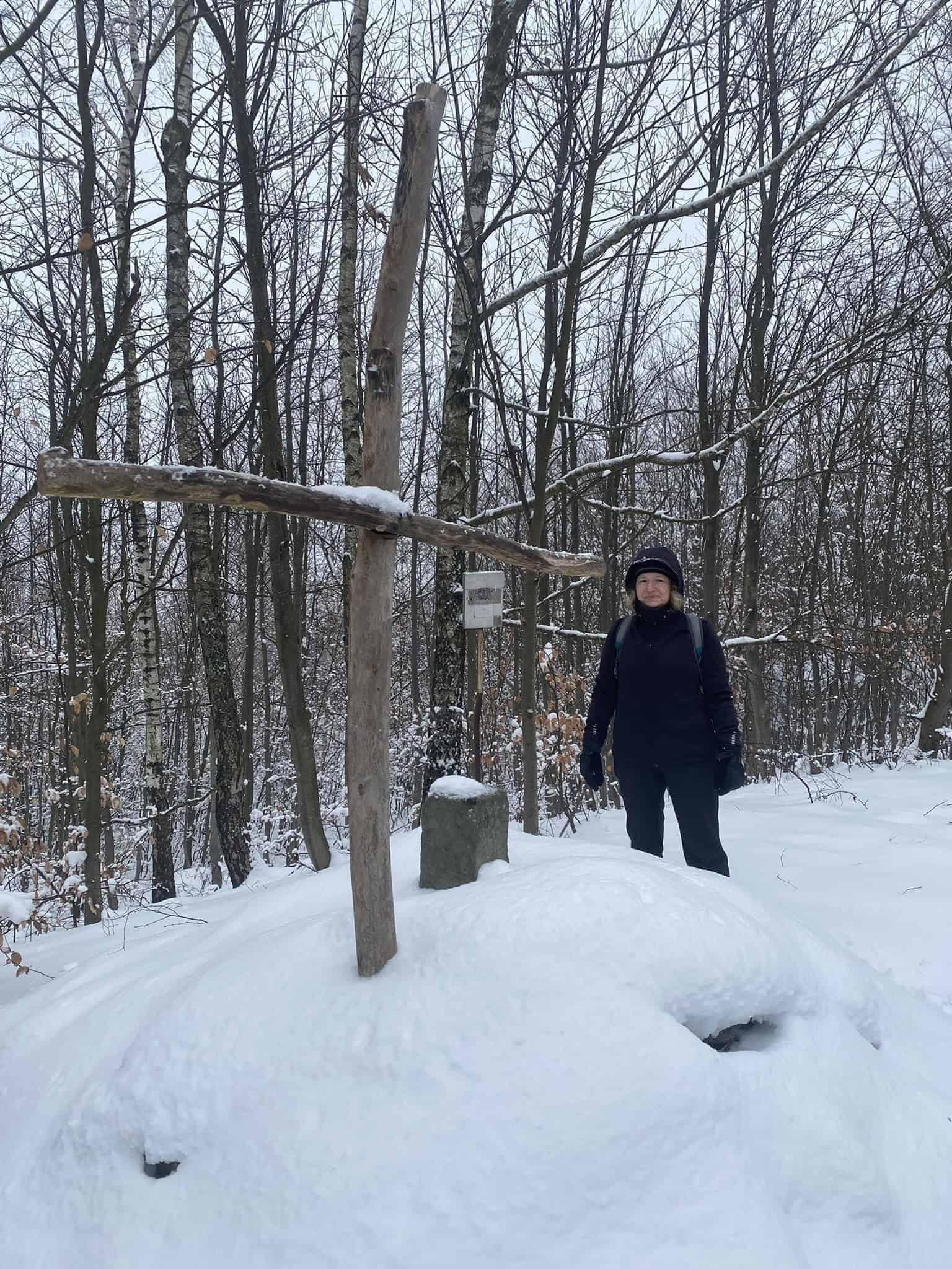 Kus historie zasazený v tichém zimním lese v podobě prostého dřevěného kříže.