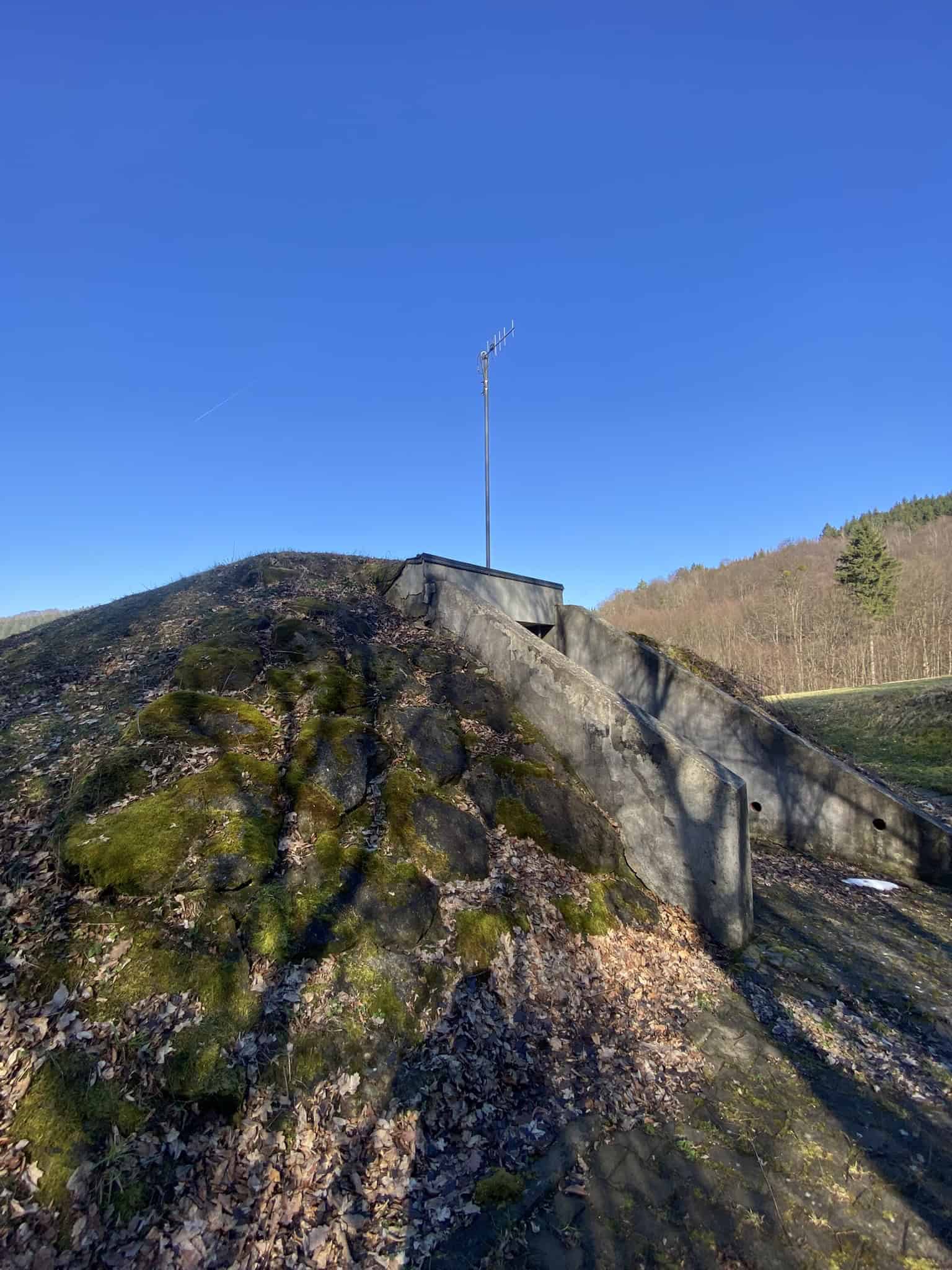 Záhadný betonový bunkr zarostlý mechem s funkční anténou.